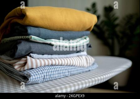 Stack of folded clothes on ironing board at home Stock Photo