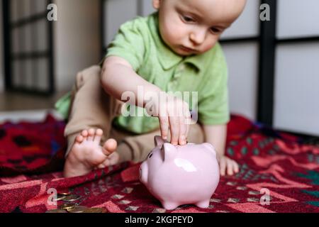 Baby boy putting coin in piggy bank Stock Photo