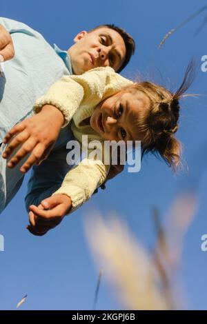 Father carrying daughter upside down under blue sky Stock Photo