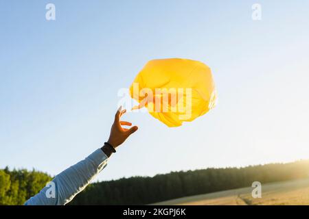 Hand of man reaching towards garbage bag balloon at field Stock Photo