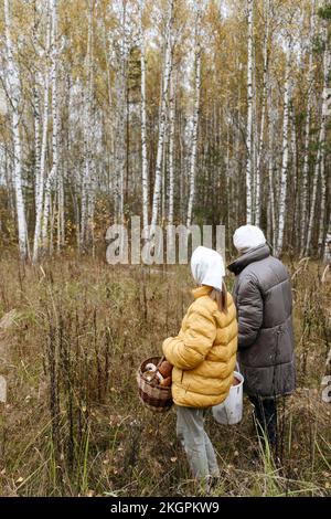 Senior woman with granddaughter collecting mushrooms in forest Stock Photo