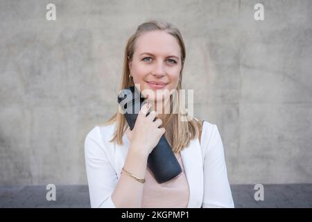 Smiling woman with reusable water bottle in front of wall Stock Photo