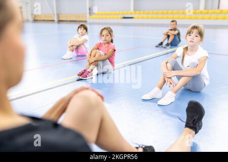 Elementary students looking at teacher teaching exercises sitting at school sports court Stock Photo