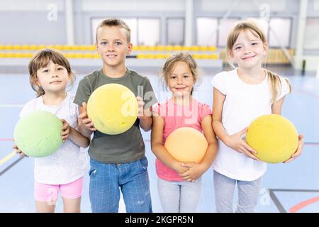 Smiling elementary students with ball standing side by side at school sports court Stock Photo