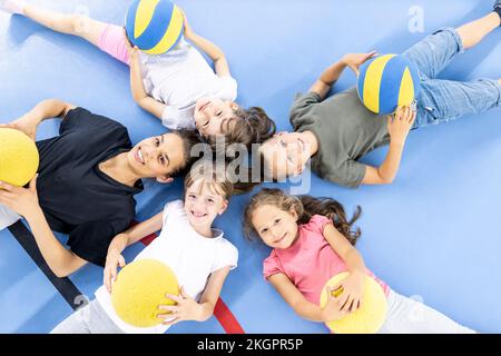 Students and teacher with ball lying down together at school sports court Stock Photo