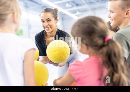Teacher talking to students holding ball at school sports court Stock Photo