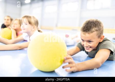 Smiling elementary boy looking at ball lying down at school sports court Stock Photo
