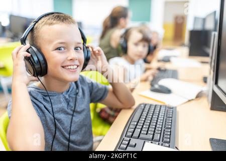 Smiling boy wearing wired headphones in computer class at school Stock Photo