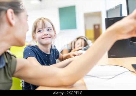 Smiling girl looking at teacher teaching in E-learning class Stock Photo