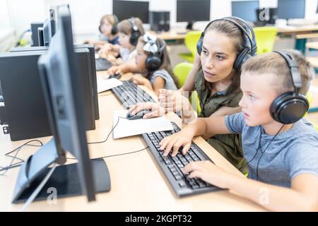 Teacher gesturing by student wearing headphones doing E-learning at school Stock Photo