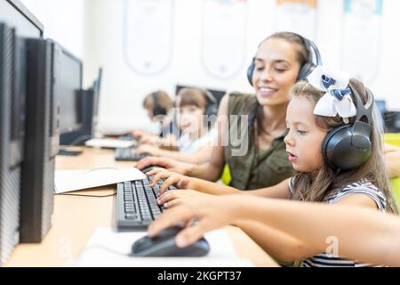 Girl wearing headphones using computer with teacher in class at school Stock Photo