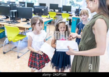 Teacher with books talking to students in classroom at school Stock Photo