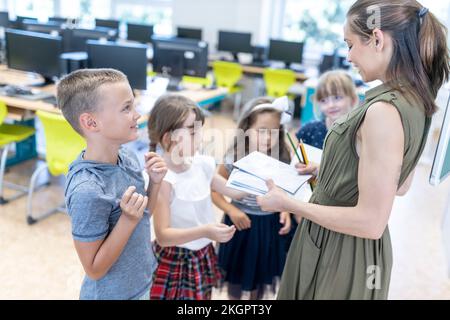 Teacher distributing notebooks to students in classroom Stock Photo