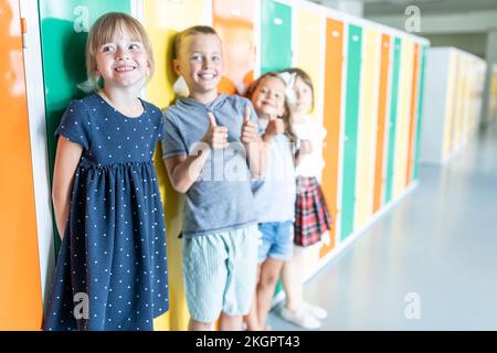 Happy elementary students standing near colorful lockers in school corridor Stock Photo