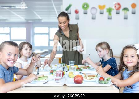 Smiling school students having lunch together with teacher at cafeteria Stock Photo