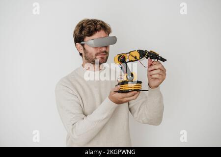 Engineer examining robotic arm wearing VR goggles in front of white wall Stock Photo