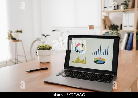 Graphs and chart on laptop screen at desk in office Stock Photo