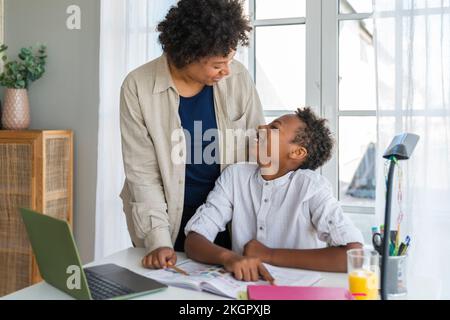 Happy mother talking to son sitting at study table in home Stock Photo