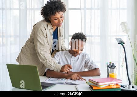 Mother assisting son studying at table in home Stock Photo