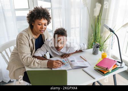 Mother assisting son doing e-learning through laptop on table at home Stock Photo