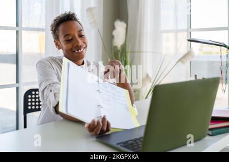 Smiling boy showing notes on video call through laptop at home Stock Photo