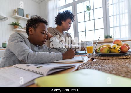 Boy making notes with mother working on laptop at home Stock Photo