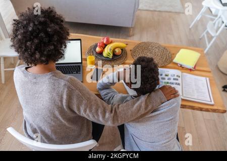Mother sitting by son doing study work at home Stock Photo