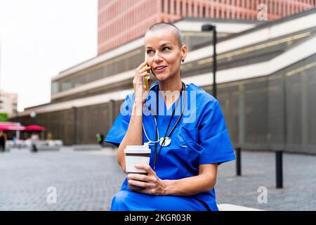 Smiling nurse with disposable coffee cup talking on mobile phone Stock Photo