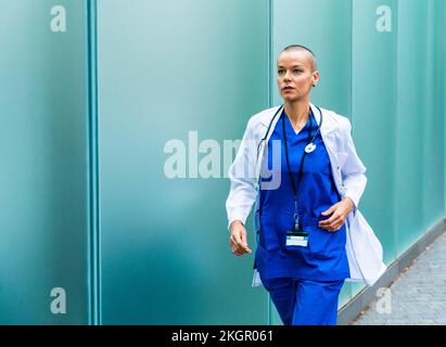 Mature doctor in lab coat running by wall on footpath Stock Photo
