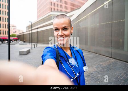 Smiling mature healthcare worker taking selfie on footpath Stock Photo