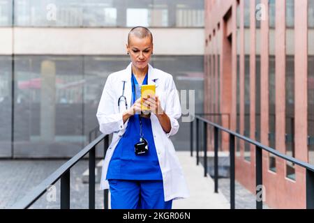 Mature doctor in lab coat using mobile phone amidst railings Stock Photo
