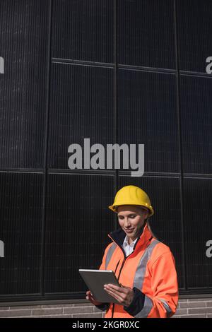 Young female engineer wearing hardhat using tablet PC in front of solar panels Stock Photo