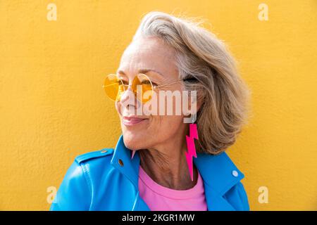 Thoughtful woman wearing sunglasses in front of yellow wall Stock Photo