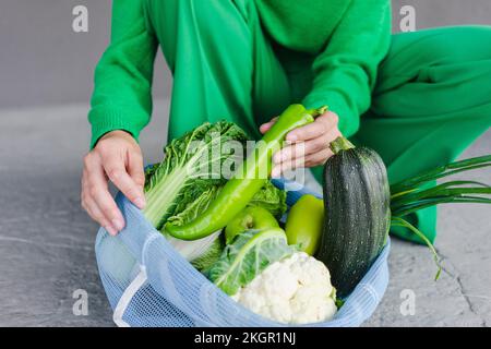 Woman putting fresh green chili pepper in mesh bag on footpath Stock Photo