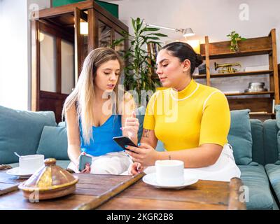 Female friends discussing over mobile phone on sofa at home Stock Photo