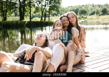 Smiling young friends with eyes closed leaning on each other at pier Stock Photo