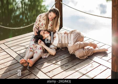 Woman talking with friend lying on lap at pier Stock Photo