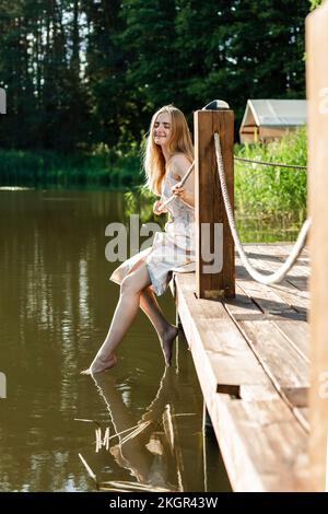 Smiling woman sitting with feet dipping in lake on pier Stock Photo