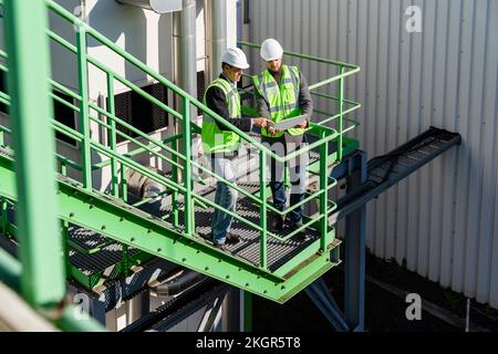 Engineers discussing over tablet PC on sunny day at recycling plant Stock Photo