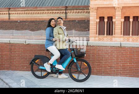 Happy mature couple sitting on electric bicycle by brick wall Stock Photo