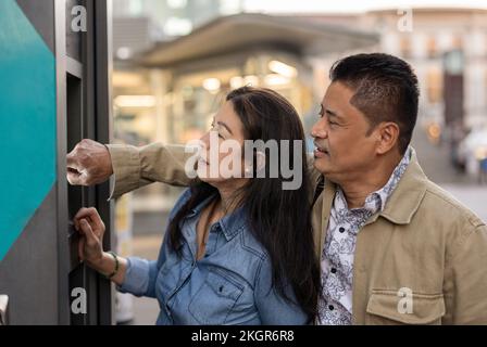Mature man using ATM machine standing with woman Stock Photo