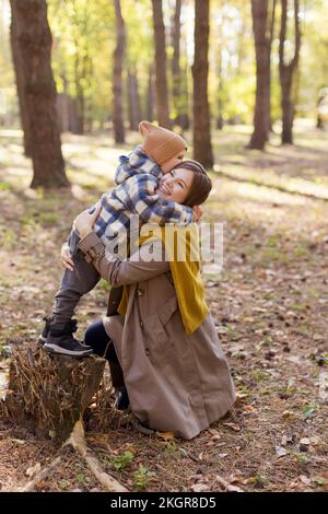Boy standing on tree stump embracing mother in park Stock Photo