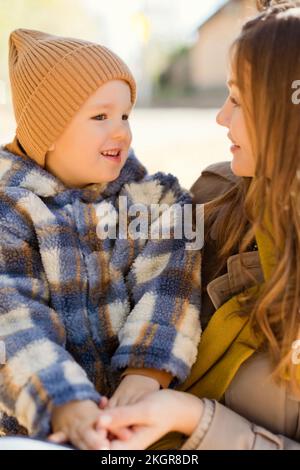 Cute boy wearing knit hat sitting on mother in park Stock Photo