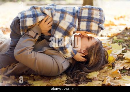 Mother kissing son lying on autumn leaves in park Stock Photo