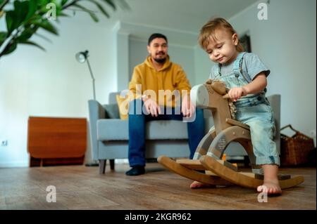 Cute boy playing on rocking horse with father in background Stock Photo