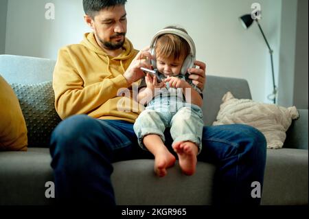 Boy using smart phone and listening to music through wireless headphones on sofa at home Stock Photo