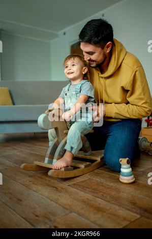 Happy boy with father playing on rocking horse at home Stock Photo