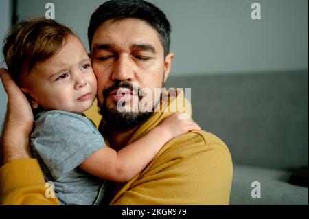 Father hugging crying son in living room at home Stock Photo