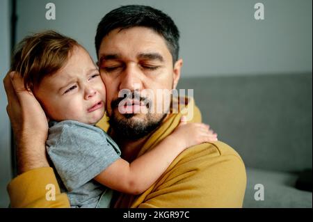 Father embracing crying son in living room at home Stock Photo