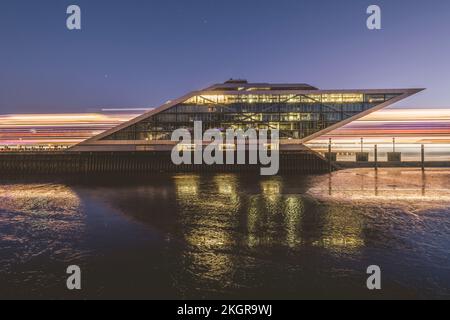 Germany, Hamburg, Dockland ferry terminal at dawn with light trails of passing ship behind Stock Photo